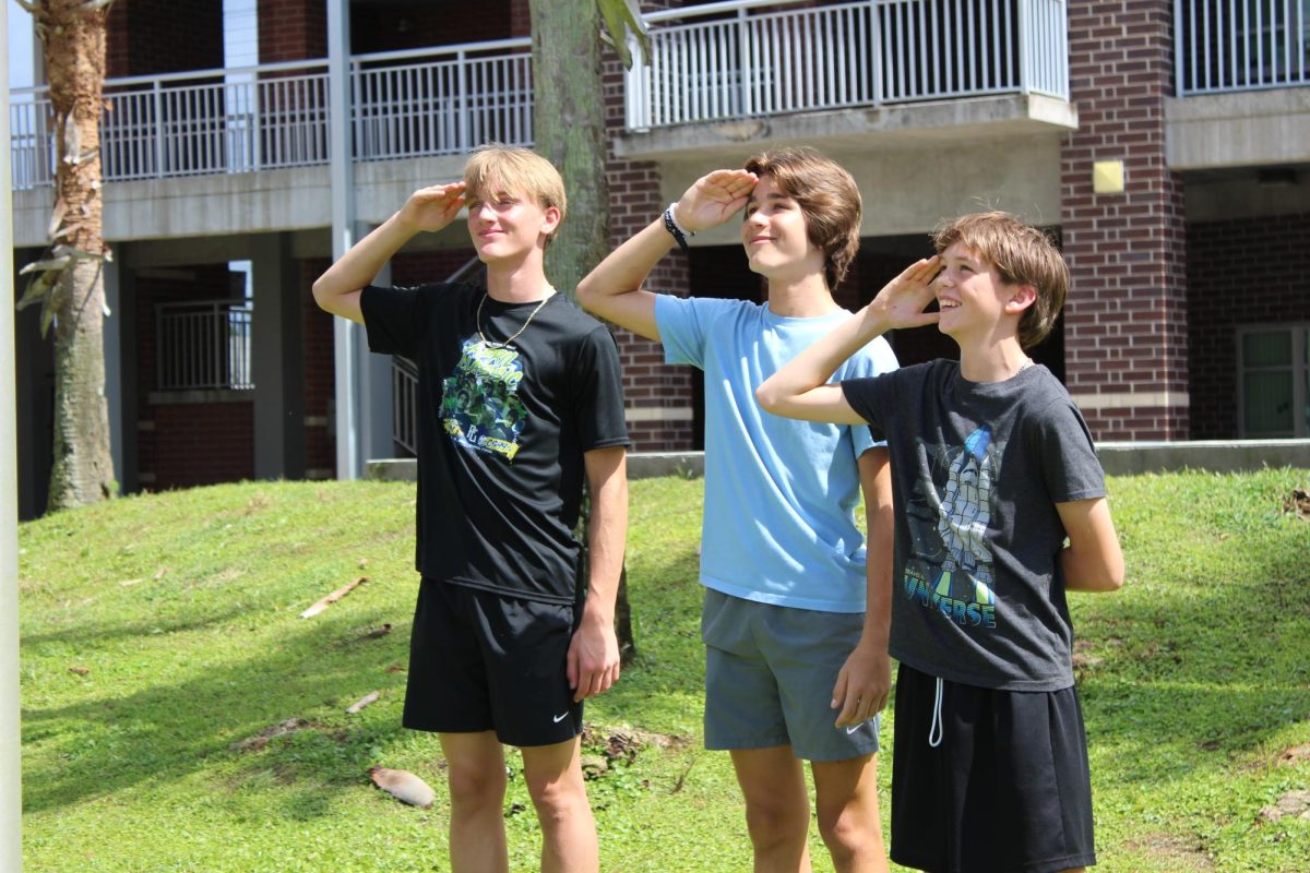 Easton Hubbard (left), Jace Mcguire-Adams (middle), and Truett Bock (right) salute the flag before taking it down.